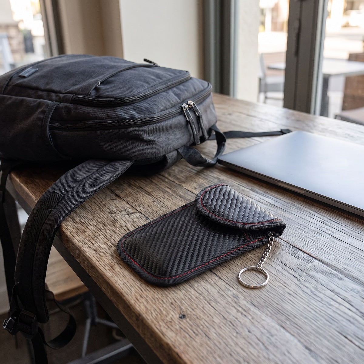 Closed KeyQuiet pouch on a cafe table beside a laptop and backpack